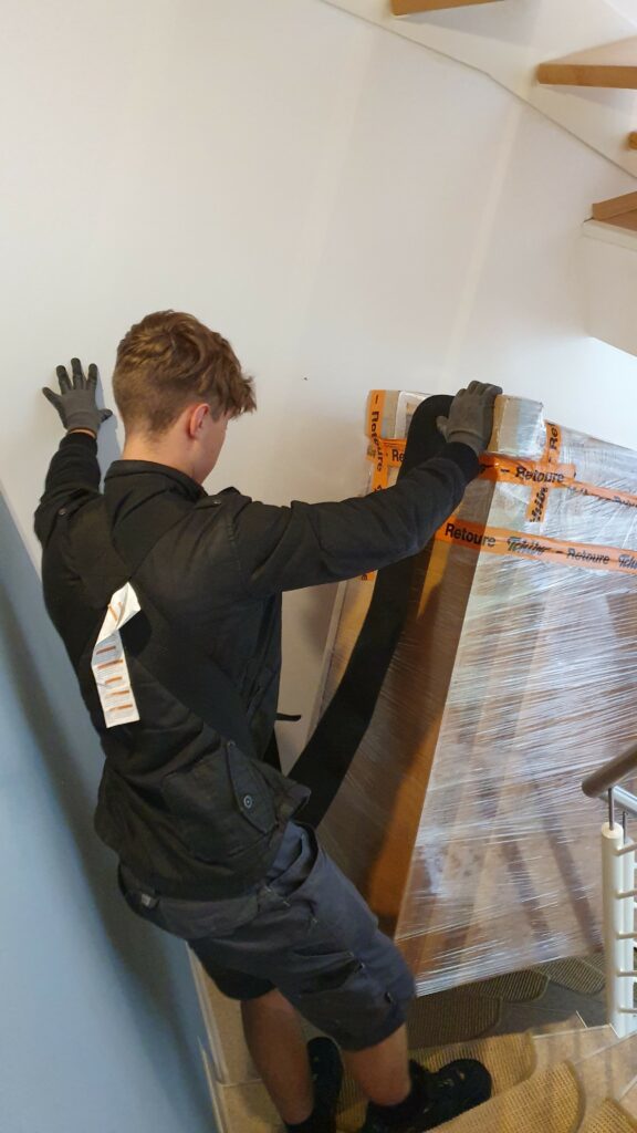 Mitarbeiter von Möbeltaxi Lüneburg tragen ein sicher verpacktes Möbelstück durch ein Treppenhaus