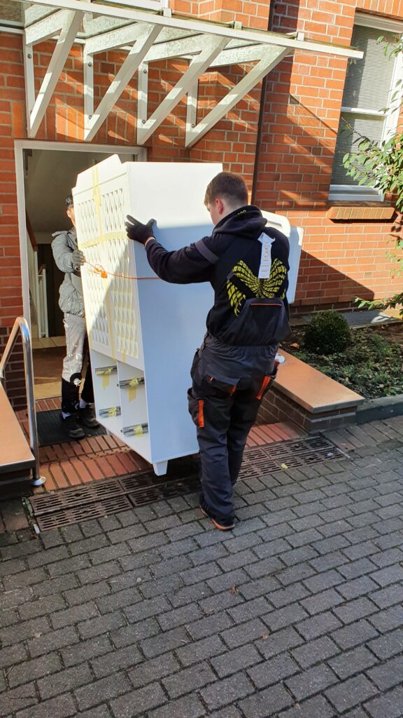 Mitarbeiter von Möbeltaxi Lüneburg transportieren eine Schrank durch eine Haustür