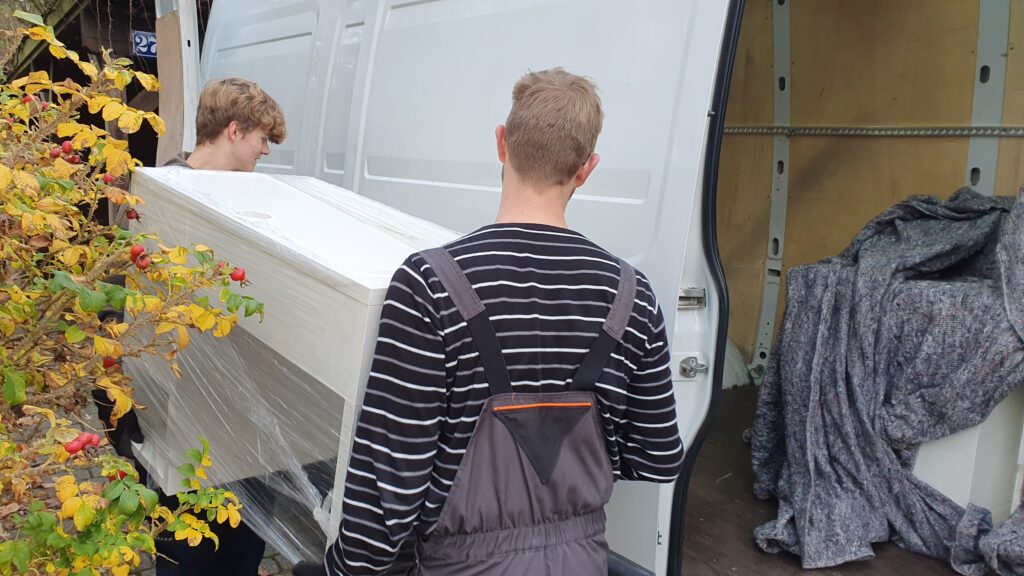 Mitarbeiter von Möbeltaxi Lüneburg transportieren einen Schreibtisch in ein Lieferfahrzeug