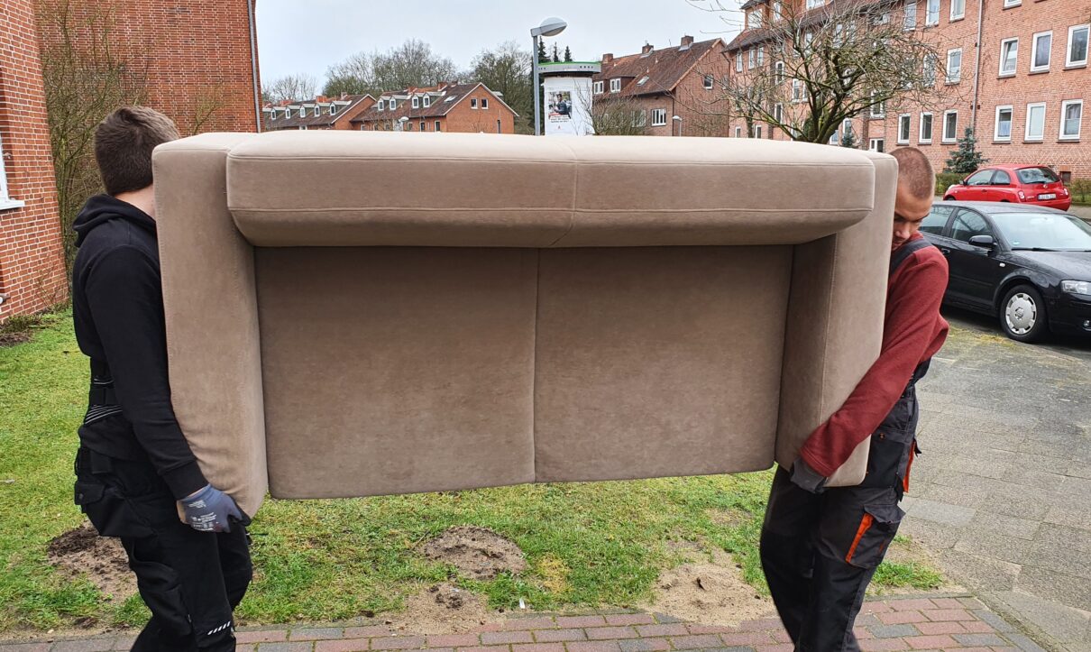 Mitarbeiter von Möbeltaxi Lüneburg tragen ein altes Sofa das entsorgt werden soll