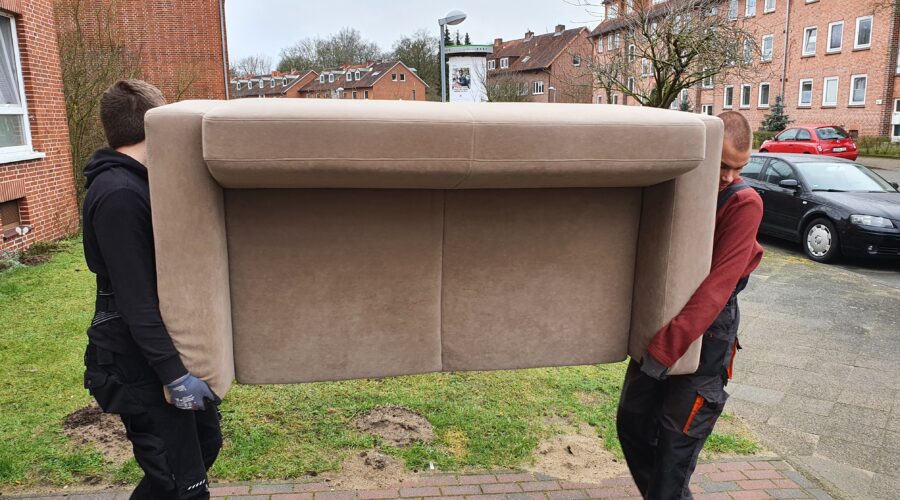 Mitarbeiter von Möbeltaxi Lüneburg tragen ein altes Sofa das entsorgt werden soll