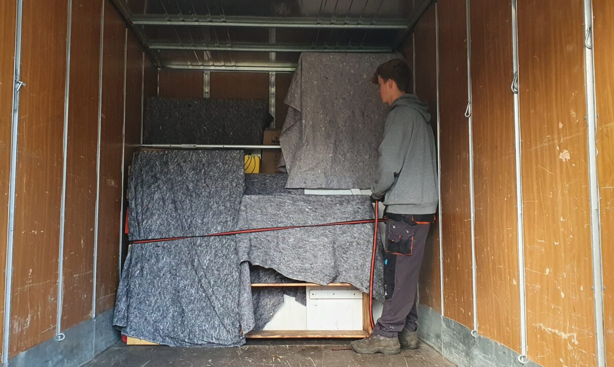 Mitarbeiter von Möbeltaxi Lüneburg sichert mit Umzugsdecken geschützte Möbel in einem LKW