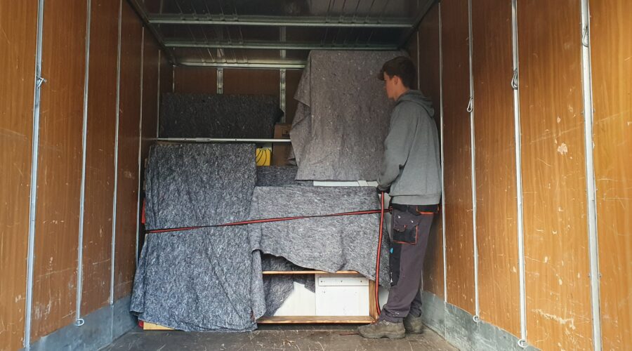 Mitarbeiter von Möbeltaxi Lüneburg sichert mit Umzugsdecken geschützte Möbel in einem LKW