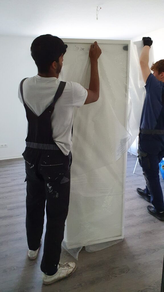 Mitarbeiter von Möbeltaxi Lüneburg verpacken ein Möbelstück in Luftpolsterfolie